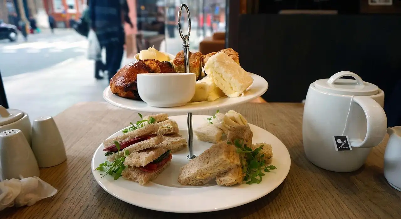 A tiered stand of finger sandwiches and cakes beside a teapot