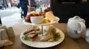 A tiered stand of finger sandwiches and cakes beside a teapot