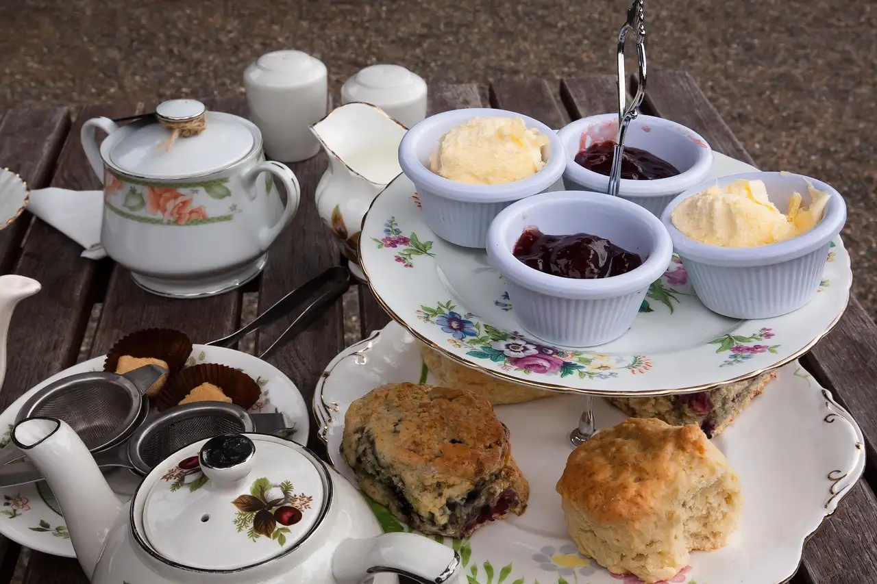 A tiered stand with scones, clotted cream and jam next to a china teapot