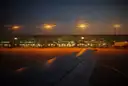 View over a plane's wing to a lit airport terminal at dusk