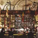 A busy bar with shelves of bottles and old penny-farthing bicycles overhead