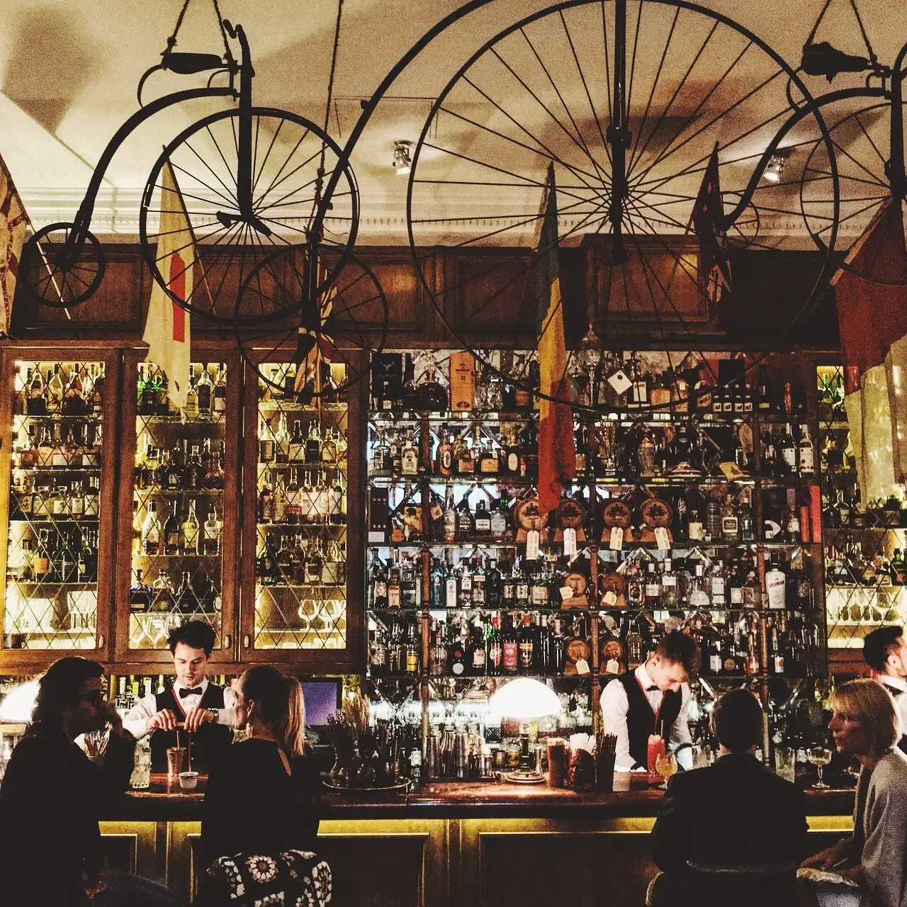 A busy bar with shelves of bottles and old penny-farthing bicycles overhead