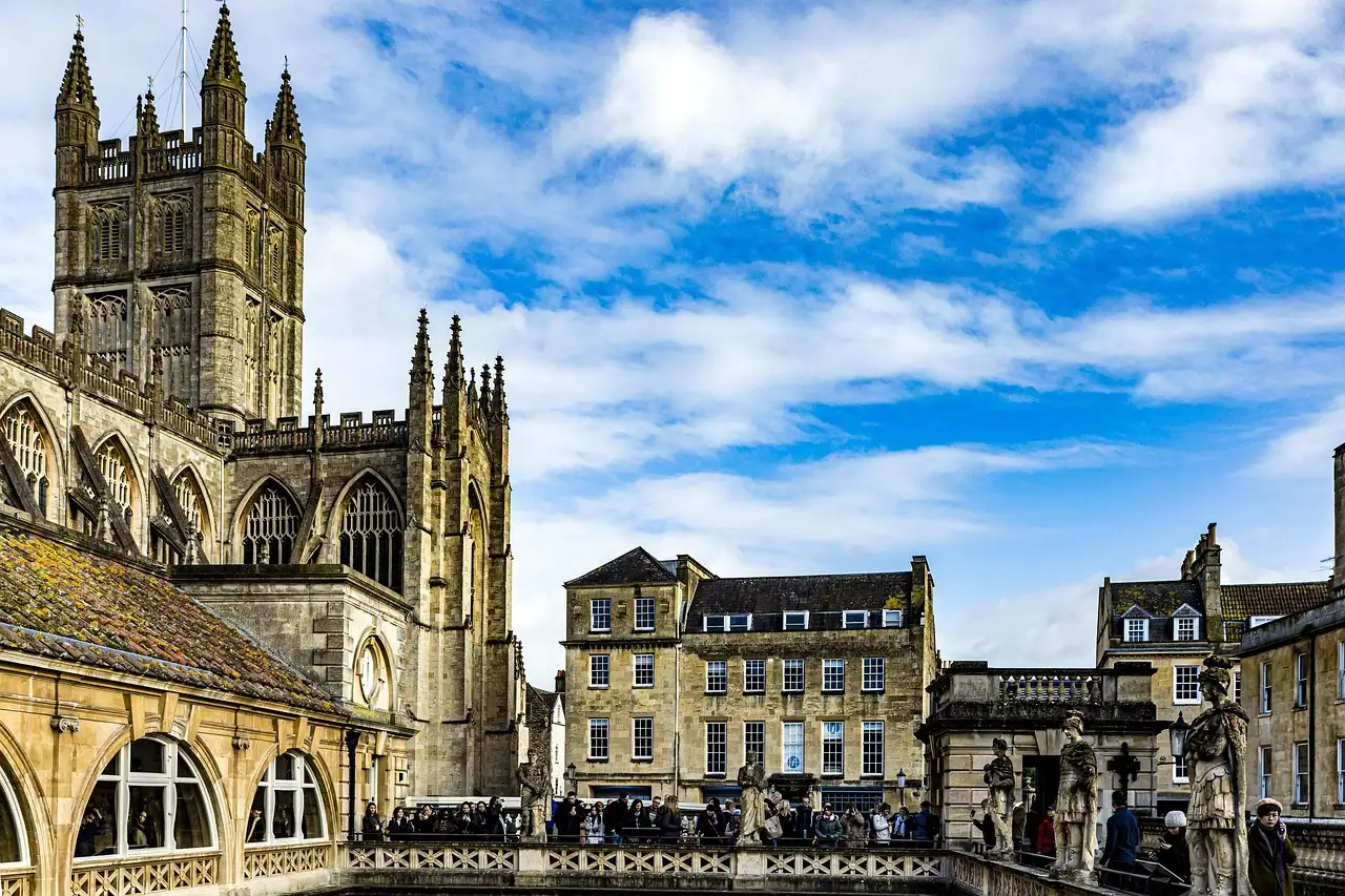 Bath Abbey's tower next to the Roman Baths building under a blue sky