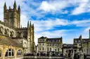 Bath Abbey's tower next to the Roman Baths building under a blue sky