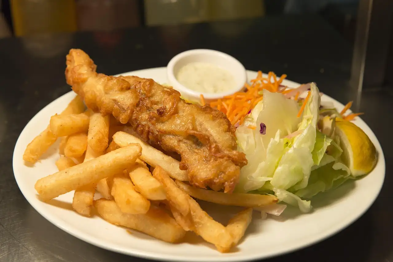 Battered fish and chips with tartare sauce and a lemon wedge on a white plate