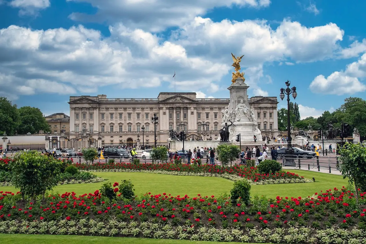 Buckingham Palace and the Victoria Memorial behind red flower beds under a blue sky