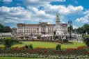 Buckingham Palace and the Victoria Memorial behind red flower beds under a blue sky