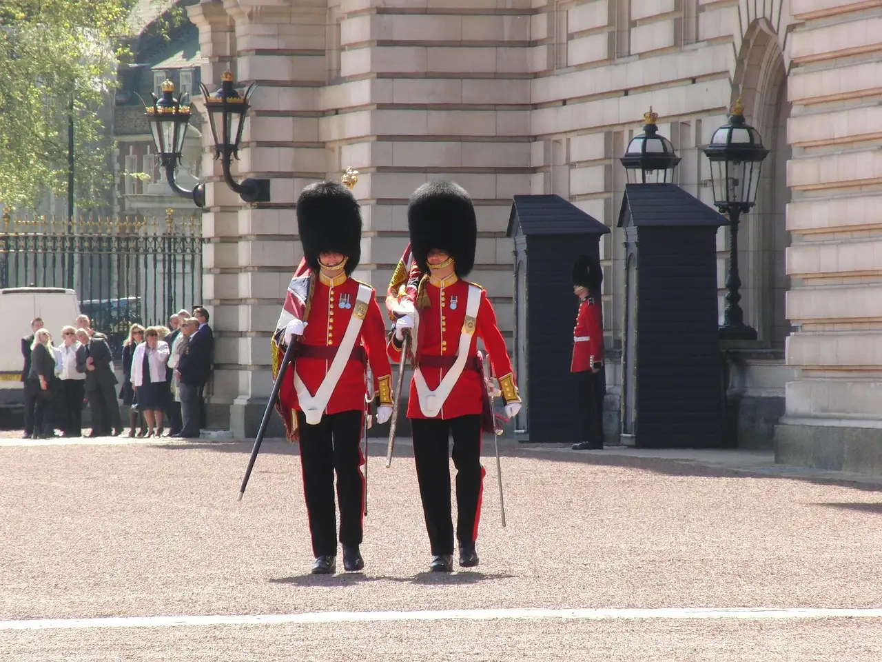 Two guardsmen in red tunics and bearskin hats beside sentry boxes at Buckingham Palace