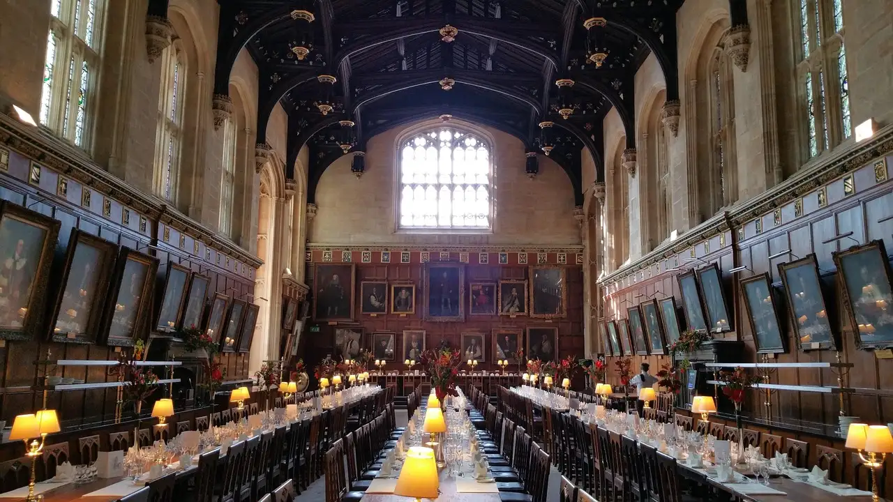 Christ Church Great Hall in Oxford with long dining tables, lamps and portraits on the walls