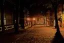 An empty cobbled street at night lit by old street lamps