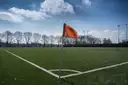 A red corner flag on a football pitch under a blue sky