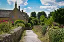 Stone cottage behind a flowering garden wall and footpath in the Cotswolds