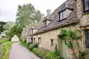 Narrow lane past stone cottages with climbing plants in a Cotswold village