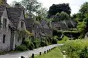 Row of stone cottages with green gardens beside a path in a Cotswold village