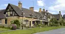 Honey-coloured stone cottages beside a grassy village green in the Cotswolds