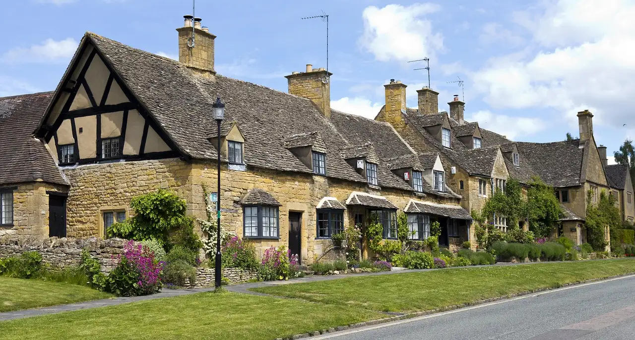 Honey-coloured stone cottages beside a grassy village green in the Cotswolds