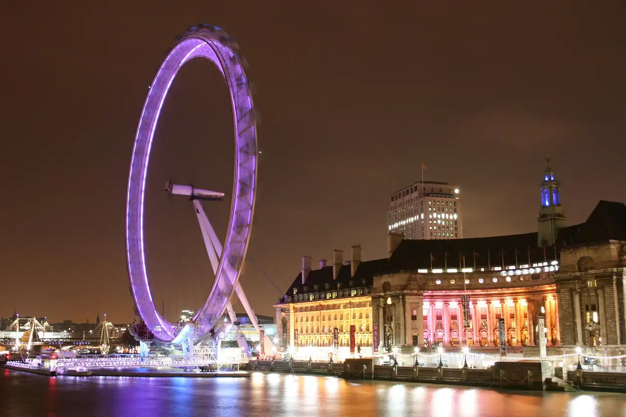 County Hall lit up at night beside the glowing London Eye on the Thames