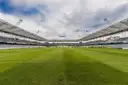An empty football stadium with a striped pitch under a cloudy sky