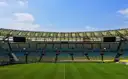 An empty football stadium in daylight with stands around the pitch