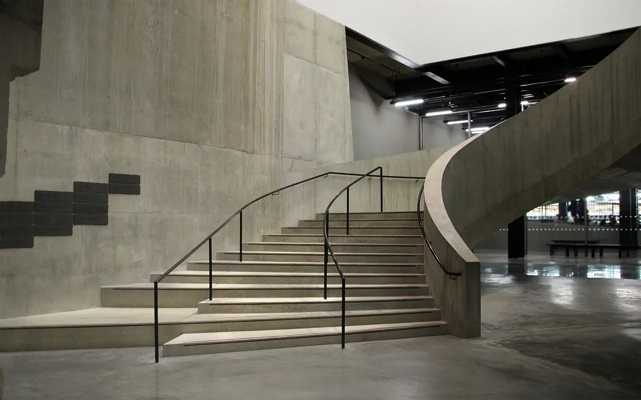A wide concrete staircase with a curved handrail rising through the bare industrial hall of a modern art museum