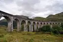 Steam train on the stone arches of the Glenfinnan Viaduct under grey clouds