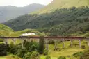 Steam train crossing the curved Glenfinnan Viaduct in a green Scottish Highland glen