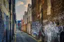 A narrow brick alley in London with graffiti on the walls