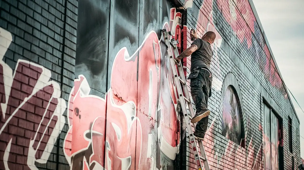 A graffiti artist on a ladder spray-painting a brick wall
