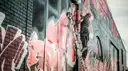 A graffiti artist on a ladder spray-painting a brick wall