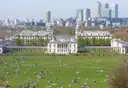 People on the lawn of Greenwich Park with the Old Royal Naval College and Canary Wharf beyond