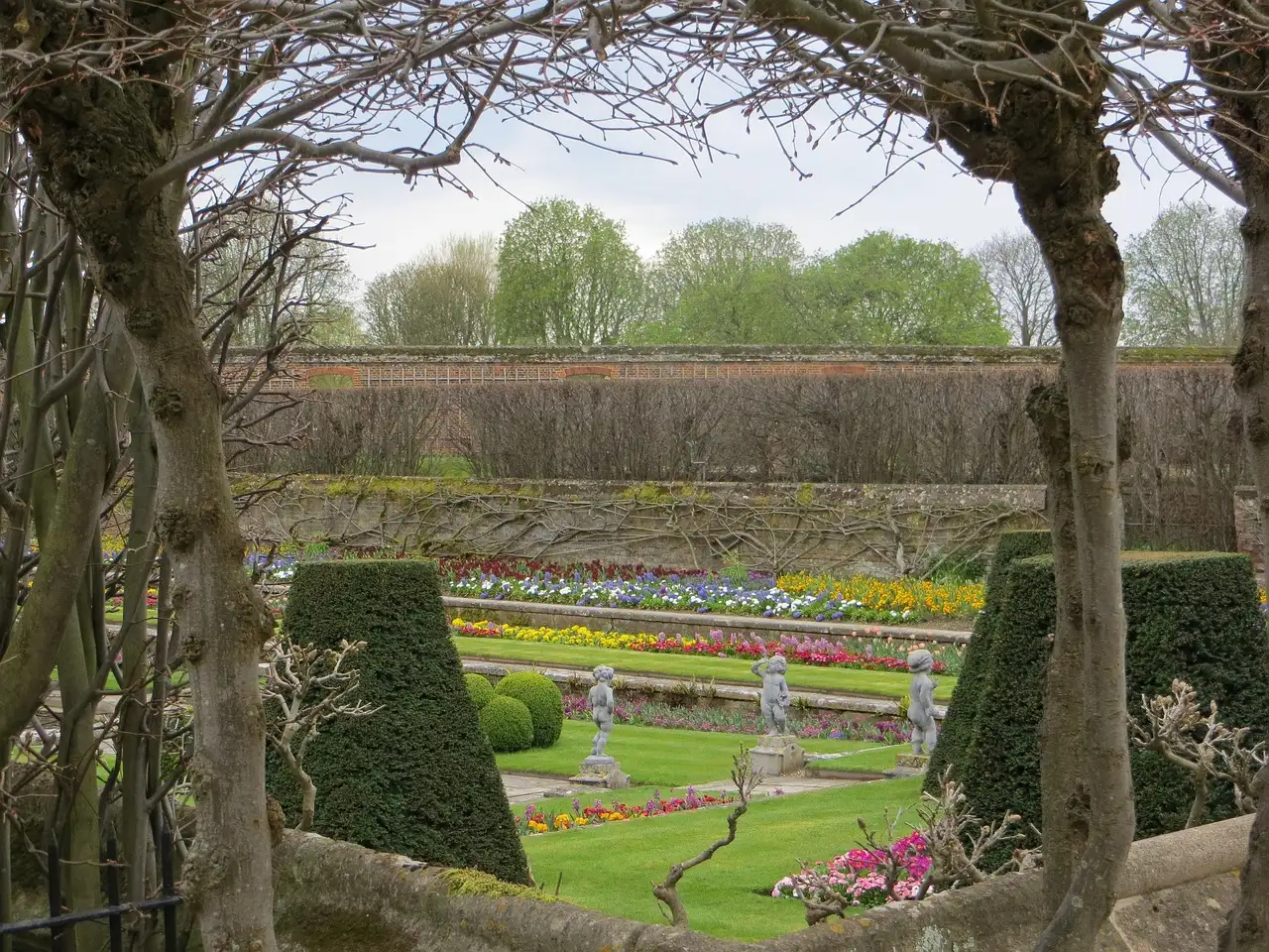 Spring flower beds in a walled garden at Hampton Court Palace, seen through an arbour