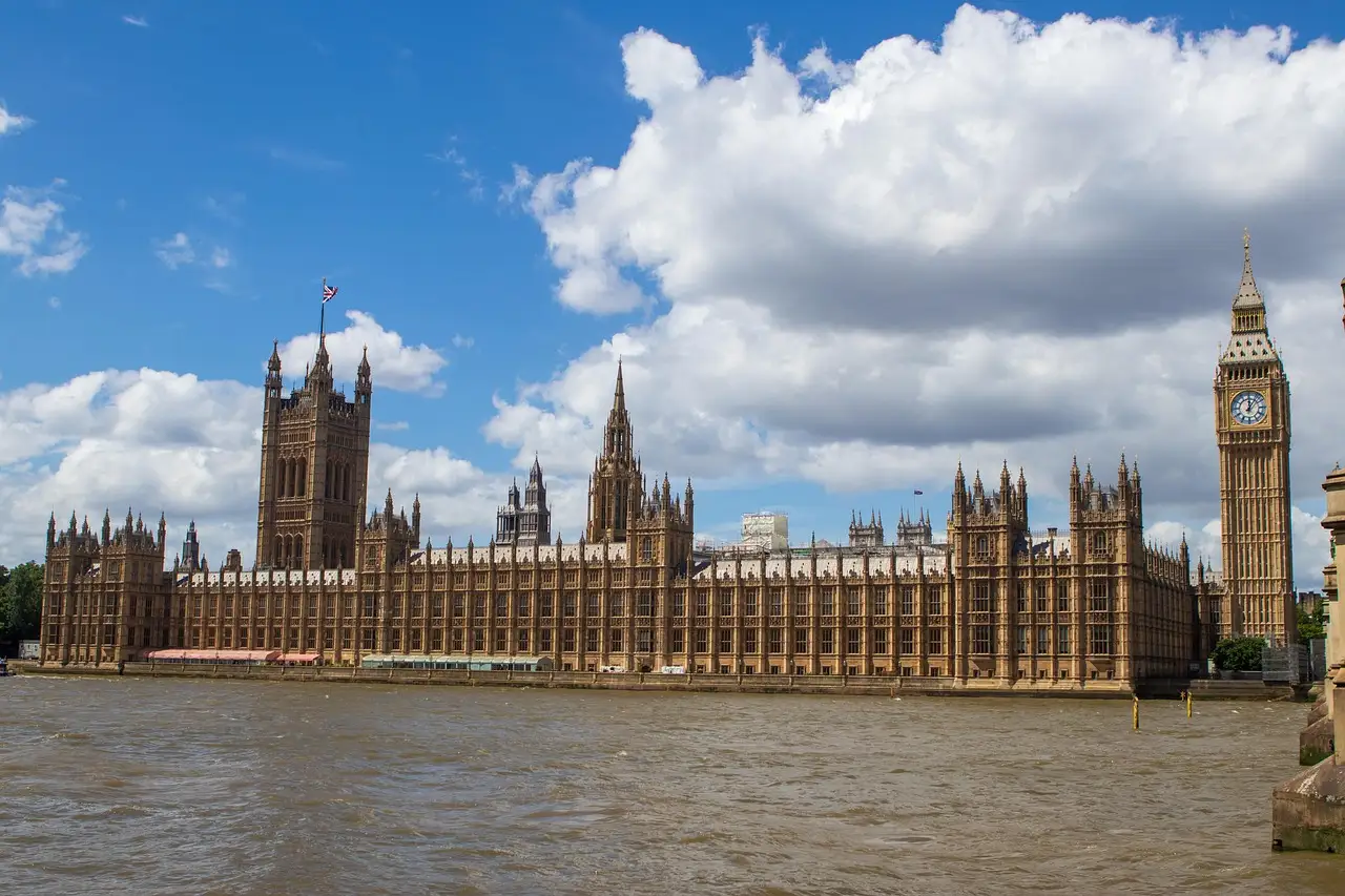 The Houses of Parliament and Big Ben beside the Thames under a blue sky with white clouds