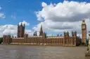 The Houses of Parliament and Big Ben beside the Thames under a blue sky with white clouds