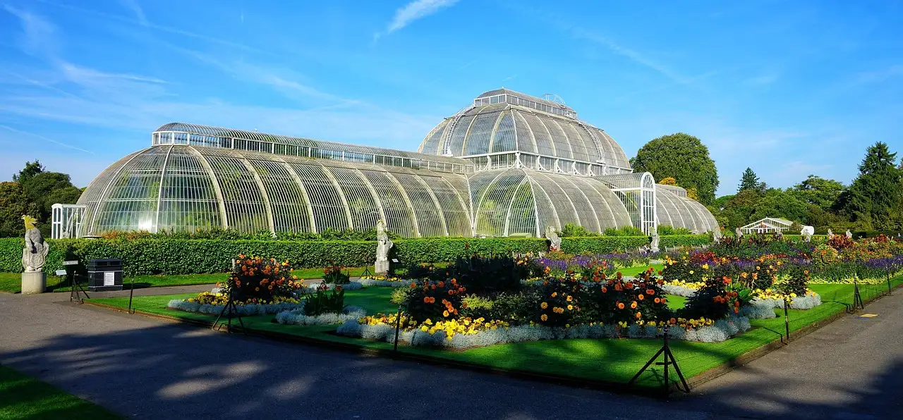 The curved glass Palm House at Kew Gardens behind colourful flower beds under a blue sky
