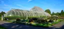 The curved glass Palm House at Kew Gardens behind colourful flower beds under a blue sky