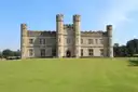 The stone towers and battlements of Leeds Castle behind a wide green lawn under a blue sky