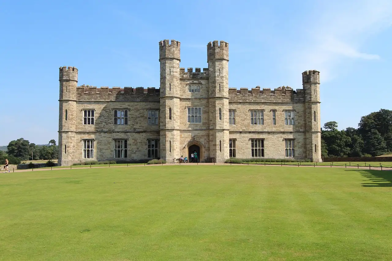 The stone towers and battlements of Leeds Castle behind a wide green lawn under a blue sky