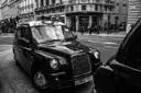 Black-and-white photo of a black London cab in a city street