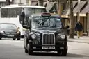 Black London taxi driving along a city street with traffic behind