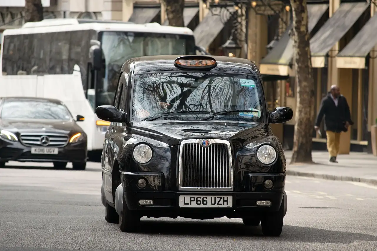 Black London taxi driving along a city street with traffic behind