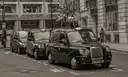 Row of black London cabs parked along a kerb in black and white
