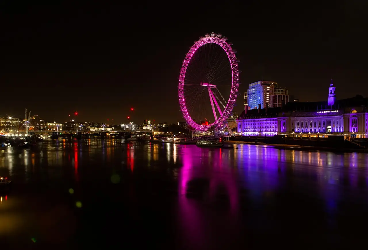 The London Eye lit pink at night, reflected in the Thames