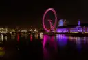 The London Eye lit pink at night, reflected in the Thames