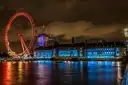 The London Eye lit red at night beside County Hall, reflected in the River Thames