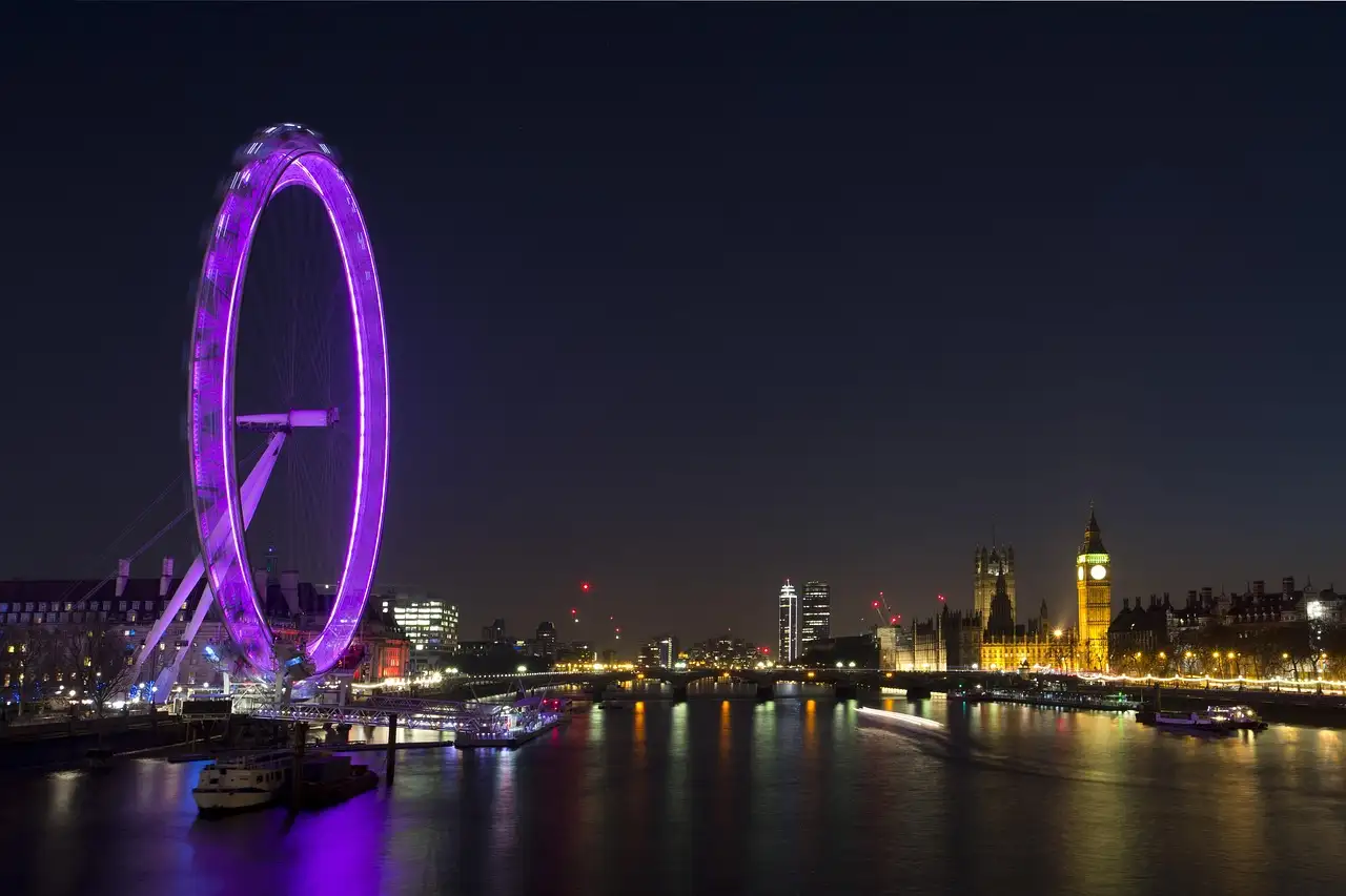 London Eye lit purple at night with Big Ben across the River Thames