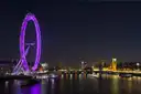 London Eye lit purple at night with Big Ben across the River Thames
