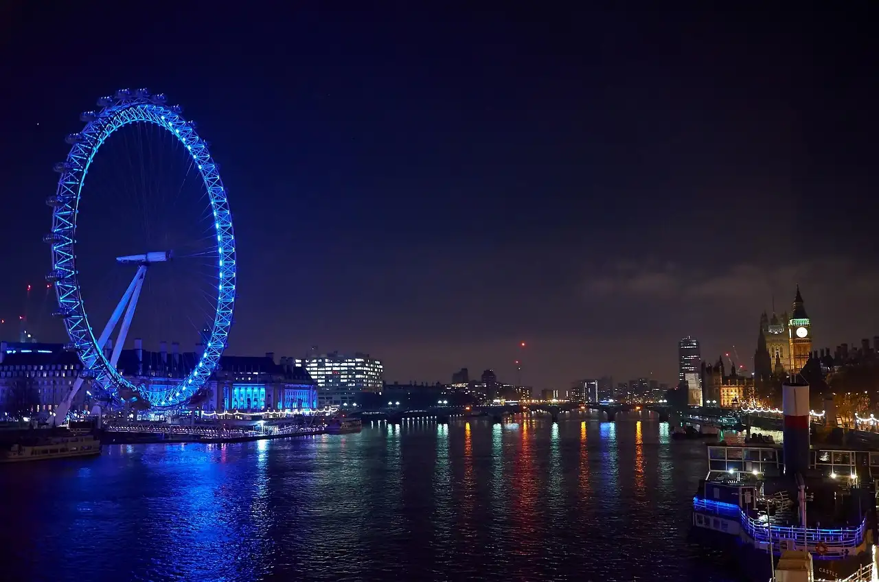 The London Eye lit blue at night, reflected in the River Thames