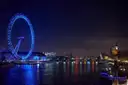 The London Eye lit blue at night, reflected in the River Thames