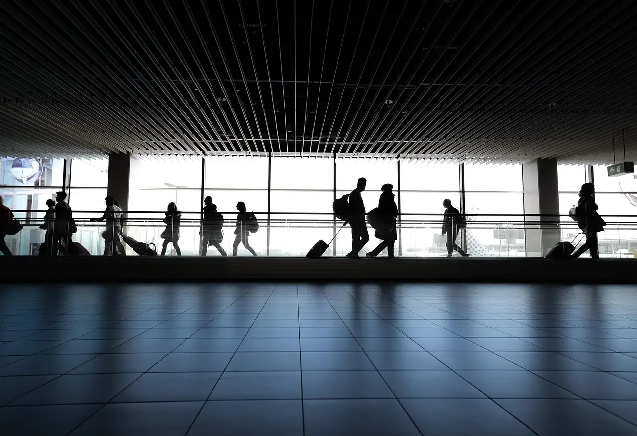 Travellers with luggage in silhouette walking along a bright airport terminal window