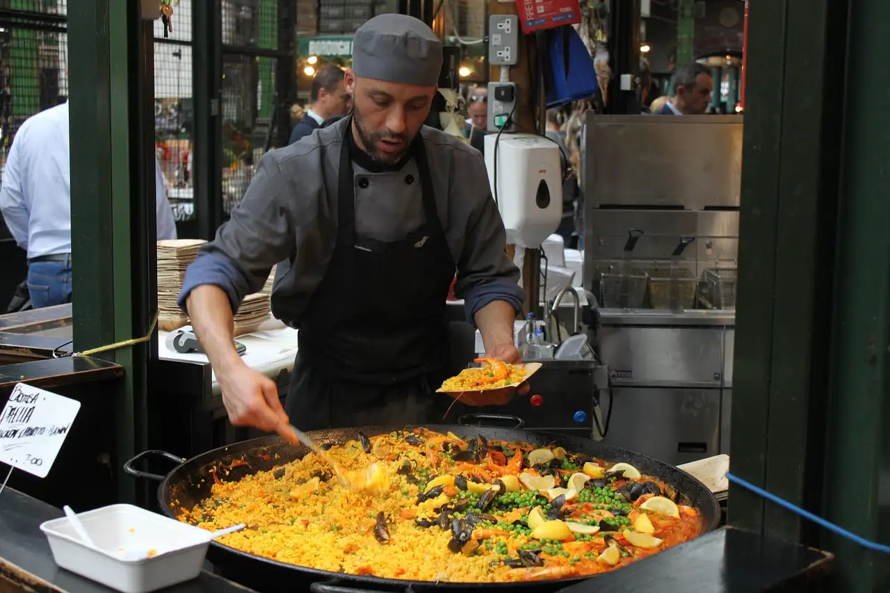 A cook serving paella from a giant pan at a London market stall